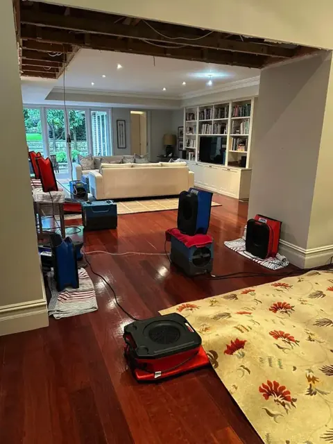 Air movers and dehumidifiers drying hardwood floors in a Temecula living room