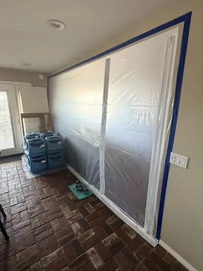 Plastic containment wall with dehumidifiers staged behind it on a tile floor
