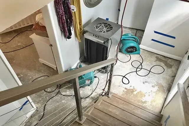 Air movers and a dehumidifier drying a stair landing and hallway after a leak