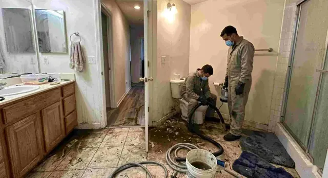 Two technicians in protective gear cleaning a bathroom after a backup